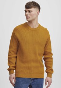 Mustard yellow ribbed knit sweater with a crew neck, long sleeves, and a relaxed fit. Notable texture and even stitching detail.
