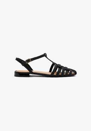 Sandal con cinturino slingback intrecciato nero, design a T, suola piatta e un accento nero lucido sul tallone. Presenta punta aperta e texture intrecciata.