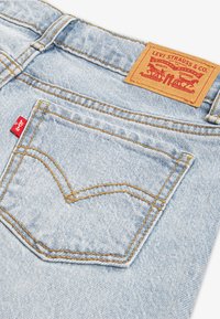 Lyseblå denimjeans med en sydd lomme og et brunt skinnmerke med påskriften "Levi Strauss & Co." Utsmykket med gule sømmer.