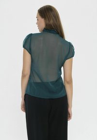 Teal sheer blouse with short puff sleeves and a ruffled neckline. The design features a slightly loose fit and smooth texture.
