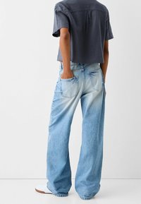 Szerokie, jasnoniebieskie dżinsy z wyblakłym wzorem, z przednimi i tylnymi kieszeniami, noszone z krótkim ciemnoszarym topem.