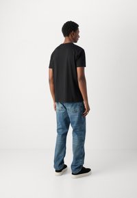 T-shirt noir à manches courtes avec un col rond, porté avec un jean droit bleu clair et des baskets noires avec une semelle blanche.