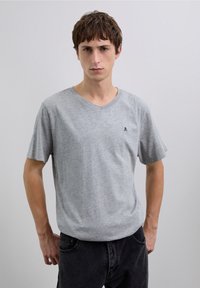 Graues, kurzärmeliges V-Ausschnitt-T-Shirt aus weichem Stoff; verfügt über ein kleines schwarzes Logo auf der linken Brustseite und eine lockere Passform.