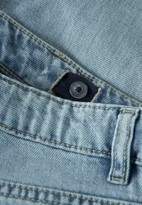 Jasnoniebieska tkanina dżinsowa z kontrastującym żółtym przeszyciem, prezentująca metalowy guzik oraz złożony pas z teksturowaną powierzchnią.