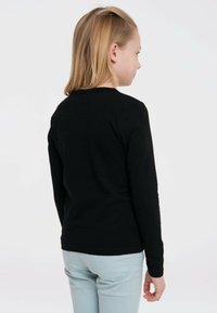 Schwarzes Langarmshirt aus weicher Baumwolle, mit einem klassischen Rundhalsausschnitt und einer figurbetonten Passform, getragen mit hellblauen Jeans.