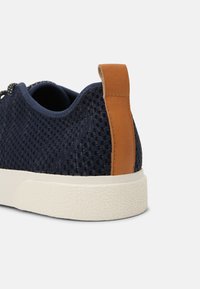 Marineblaue Mesh-Sneaker mit strukturierter Außensohle, braunem Leder-Heel-Tab und kontrastierendem cremefarbenem Zwischensohlenteil.