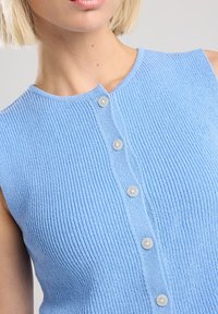 Light blue sleeveless knit top featuring a ribbed texture, round neckline, and five discrete round buttons down the front.