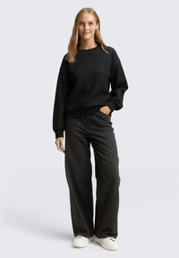 Schwarzer, strukturierter sweatshirt mit tiefen Schultern, kombiniert mit lockeren schwarzen Jeans mit metallischen Nietenakzenten und weißen Sneakern.