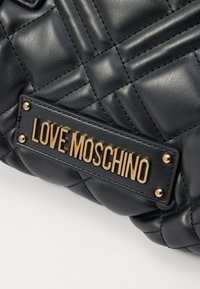 Črna prešita torbica iz teksturirane sintetične usnje; vsebuje zlato ploščico z napisom "LOVE MOSCHINO" in kovinske nete kot dodatke.