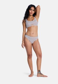White bikini set featuring a dotted pattern in dark brown, with a cropped top and low-rise bottoms. Smooth fabric and minimal detailing.