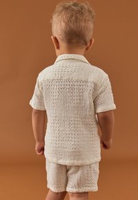 Set format din cămașă cu mânecă scurtă și pantaloni scurți texturat alb, cu un model tip vafă și guler cu nasturi, văzut din spate.