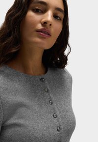 Szary sweter z dzianiny z zaokrąglonym dekoltem, z sześcioma ciemnymi guzikami na przodzie, gładką teksturą i dopasowanym fasonem.