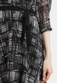 Abito a fantasia in bianco e nero con vestibilità ampia, maniche lunghe e cintura con lacci. Tessuto texturizzato con linee e forme geometriche.