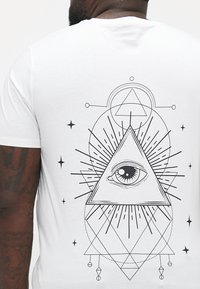 Weißes T-Shirt mit einem schwarzen geometrischen Design, das ein Auge innerhalb eines Dreiecks zeigt, umrahmt von Strahlen und dekorativen Elementen.