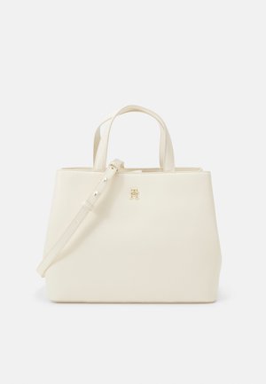 Krémová taška na rameno vyrobená z hladkého syntetického materiálu, s dvoma hornými držadlami, nastaviteľným popruhom a zlatým logom ako akcentom.