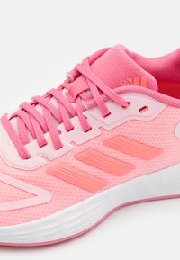 Zapatilla deportiva de color rosa claro con parte superior de malla texturizada, ojales reforzados y suela de goma. Presenta un diseño elegante y acentos en contraste.