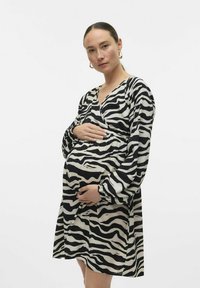 Robe de maternité noire et blanche à rayures zèbre avec manches longues, décolleté en V et taille froncée, portée par une personne tenant son ventre.