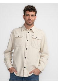 Beige Cord-Shirt mit Knopfverschluss, zwei Brusttaschen und schwarzen Knopfakzenten. Mit Kragen und langen Ärmeln gestaltet.