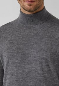 Man in een grijze gebreide turtleneck trui, zicht op de bovenste borst en de onderkant van het gezicht met lichte baardstoppels.