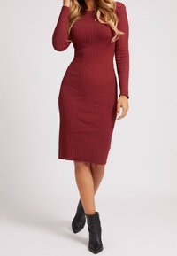Abito midi a costine di colore bordeaux, con maniche lunghe e silhouette aderente. Abbinato a stivaletti neri alla caviglia, che mettono in risalto la texture e il design.