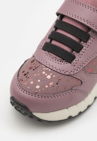 Baskets en cuir rose avec des lacets noirs, dotées d'accents métalliques éparpillés sur la zone des orteils et d'une semelle en caoutchouc noir texturé.