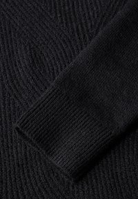 Schwarzer Strickpulloverstoff, der ein strukturiertes Muster mit erhabenen Linien zeigt. Der Bund ist gerippt, was dem Gesamtdesign zusätzliche Details verleiht.