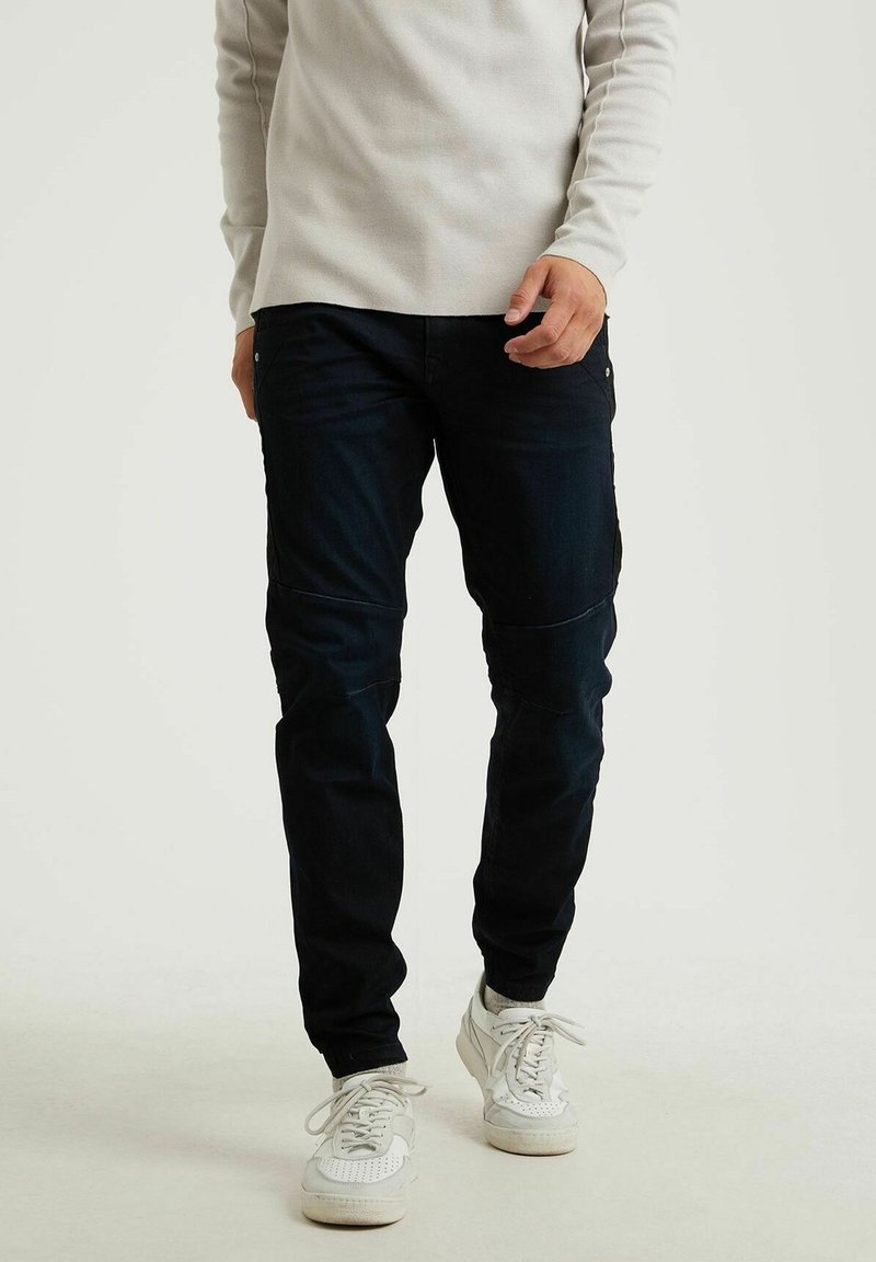 Granatowe dżinsy o slim fit, wykonane z materiału denim. Oferują minimalne przeszycia i pięć kieszeni. W połączeniu z białymi trampkami.