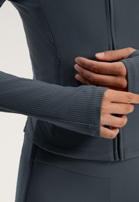 Temno siva športna jakna z rebrasto teksturo, z zadrgo spredaj in dolgimi rokavi; podrobno šivanje in oprijet kroj, idealna za aktivno nošenje.