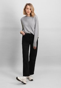 Maglione grigio chiaro con scollatura rotonda, pantaloni neri a gamba larga e sneakers bianche con suola texturizzata. Design semplice e moderno.