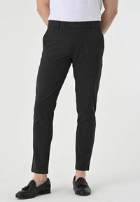 Slim-fit tailored pants made of dark textured fabric; features belt loops, button closure, and side pockets; worn with black loafers.