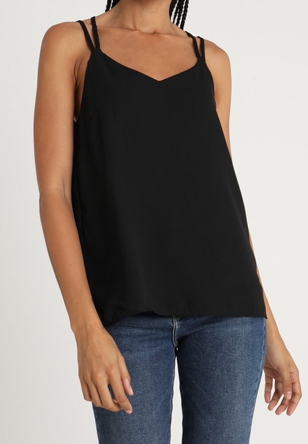 Top sans manches noir avec un décolleté en V, en tissu lisse, doté de fines bretelles et d'une coupe décontractée, associé à un jean bleu.