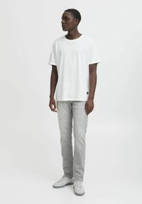 Camiseta blanca de manga corta, con cuello redondo y corte relajado; combinada con jeans rectos de color gris claro y zapatillas grises con detalles blancos.