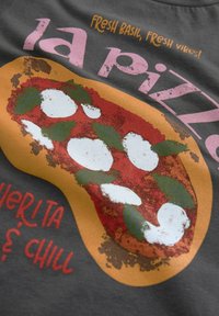T-shirt graphique présentant un design de pizza avec de la mozzarella, du basilic et des tomates sur un fond gris foncé. Le texte indique "Basilic frais, bonnes ondes !"