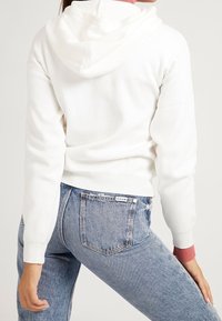 Felpa bianca a maniche corte con un finish testurizzato e un tocco di rosa nei polsini, abbinata a jeans high-waisted blu chiaro con un'etichetta logo.