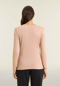 Maglione a maniche lunghe in beige chiaro, realizzato in tessuto morbido. Caratterizzato da un collo rotondo e un design aderente, abbinato a pantaloni neri.