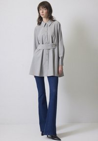 Grå skjorta med knyte i midjan, långa ärmar och en dekorativ nål. Matchad med vida mörk denimjeans och svarta klackar.