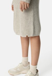 Hellgraues, geripptes Kleid in Kniehöhe, mit einem Logotag am Saum. Kombiniert mit weißen Sneakern und cremefarbenen Kniestrümpfen.