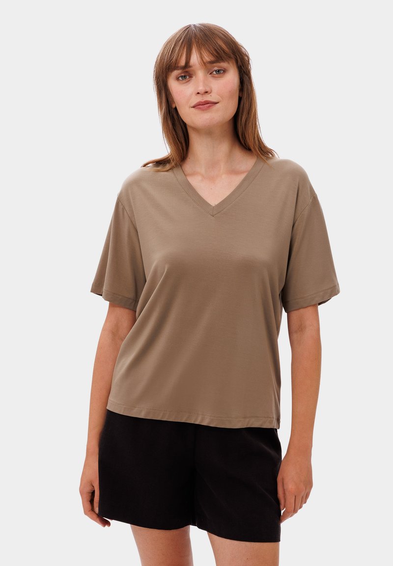 T-shirt s výstřihem do V a krátkým rukávem v béžové barvě, vyrobený z měkké tkaniny. V kombinaci s černými kraťasy, které mají volný střih a hladkou texturu.