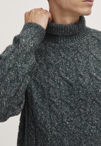 Dunkelgrüner Strickpullover mit hohem Kragen, mit einem strukturierten Rautenmuster und gerippten Bündchen. Weiches, dickes Material.