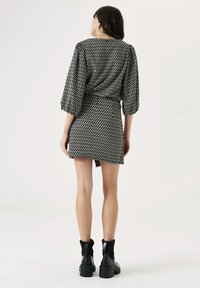 Vestido de patrón en blanco y negro con cintura ajustada y mangas abullonadas; combinado con botas de tobillo negras con acentos de punto acanalado.