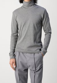 Grauer Rollkragenpullover aus weichem Stoff, mit langen Ärmeln und figurbetonter Passform. Getragen mit grauen und weißen gestreiften Hosen.