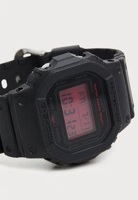 Digital G-Shock klokke med sort matte overflate, kvadratisk klokkehus, rød digital skjerm og funksjoner gravert på rammen. Vanntett design.