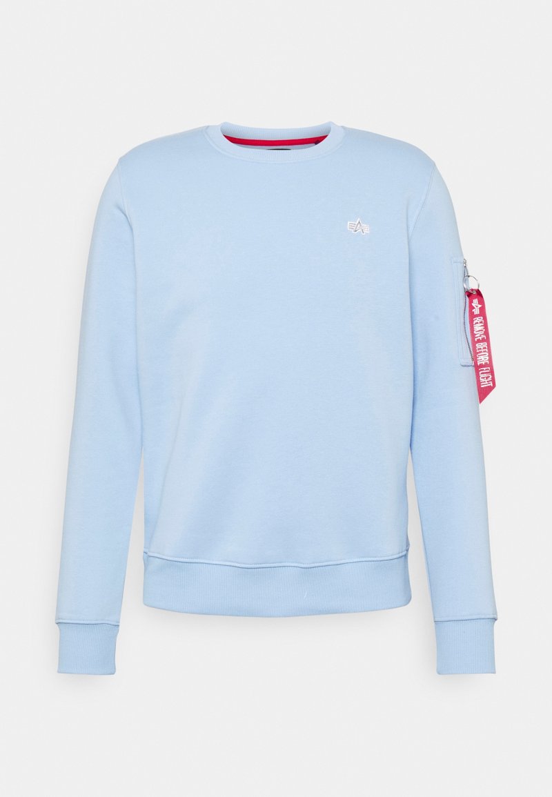 Felpa azzurra chiara in cotone morbido, con maniche lunghe, colletto rotondo e un’etichetta decorativa rosa sulla manica sinistra con del testo.
