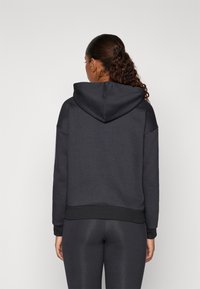 Dark gray hooded sweatshirt with a textured finish, loose fit, and ribbed hem. Paired with matching dark leggings, seen from the back.