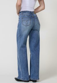 Jeans de mezclilla de pierna ancha en azul claro, que cuentan con dos bolsillos traseros con costuras decorativas y un dobladillo ligeramente deshilachado.