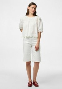 Vit kortärmad blus med scallopdetalj och ögletprydnader, matchad med vita knälånga shorts och röda skor. Enkelt mönster.