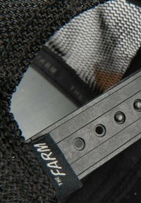 Cappellino nero in rete con tessuto strutturato, dotato di fascia regolabile in plastica e fori per la personalizzazione della taglia. L'etichetta riporta la scritta "THE FARM."