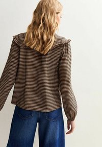 Brun och krämfärgad rutig blus med volangkrage, långärmar och textilerad tyg, i kombination med blå högmidjade denimjeans.