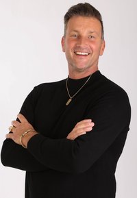 Zwarte, langmouw t-shirt met een hoge hals. Gouden sieraden accenten, waaronder een ketting en ringen, met gestructureerde afwerkingen. Neutrale achtergrond.