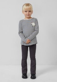 Gestreepte longsleeve shirt in crème en marine, gecombineerd met donkergrijze broek. Een bloemenaccent siert het shirt en het kind draagt zwarte schoenen.